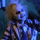 Michael Keaton as Beetlejuice, emerging from his graveyard in his iconic black and white striped suit.